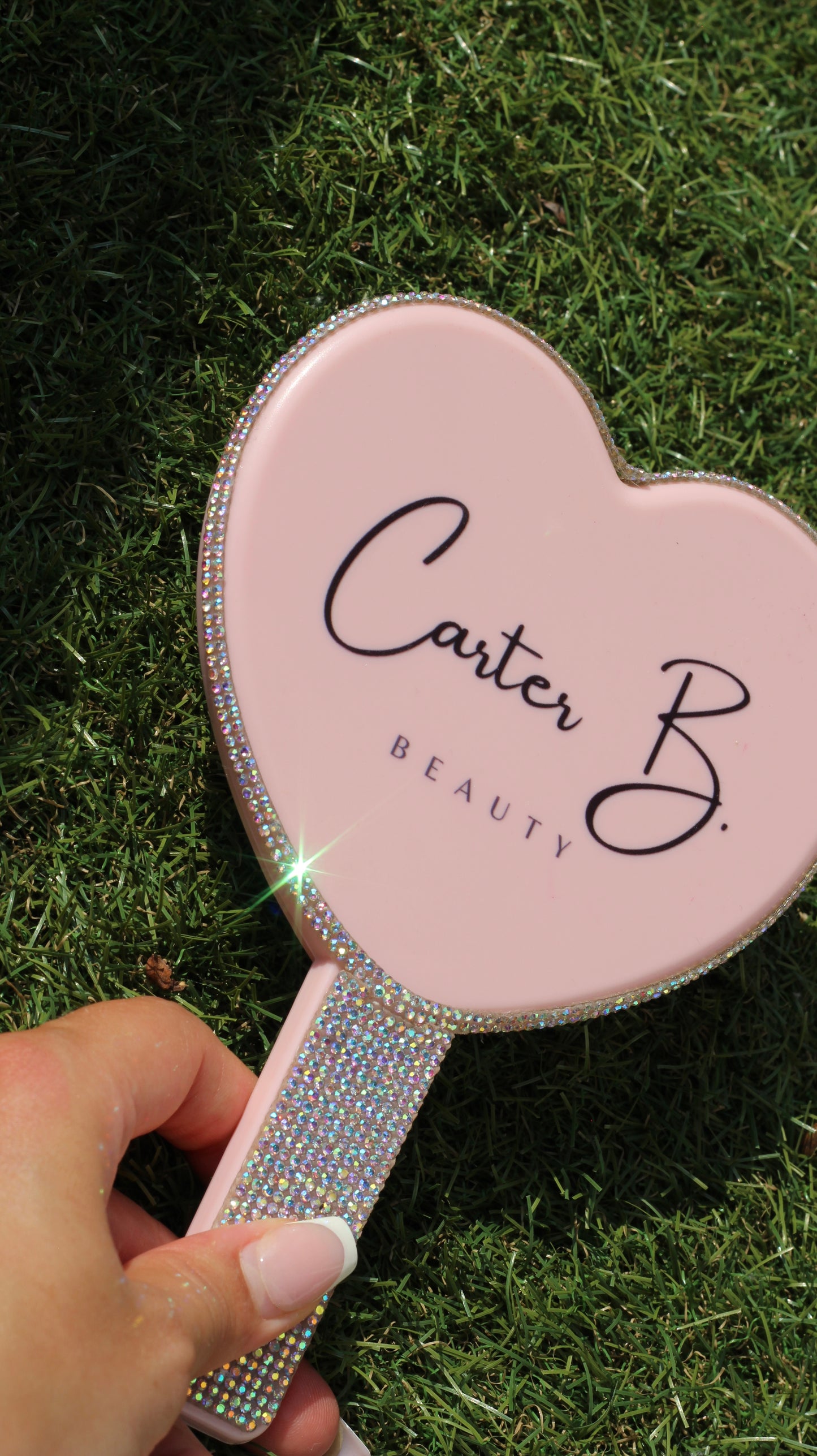 Ein herzförmiger Handspiegel, mit Glitzersteinchen besetzt (auf Kunstrasen) - von Carter B. Beauty