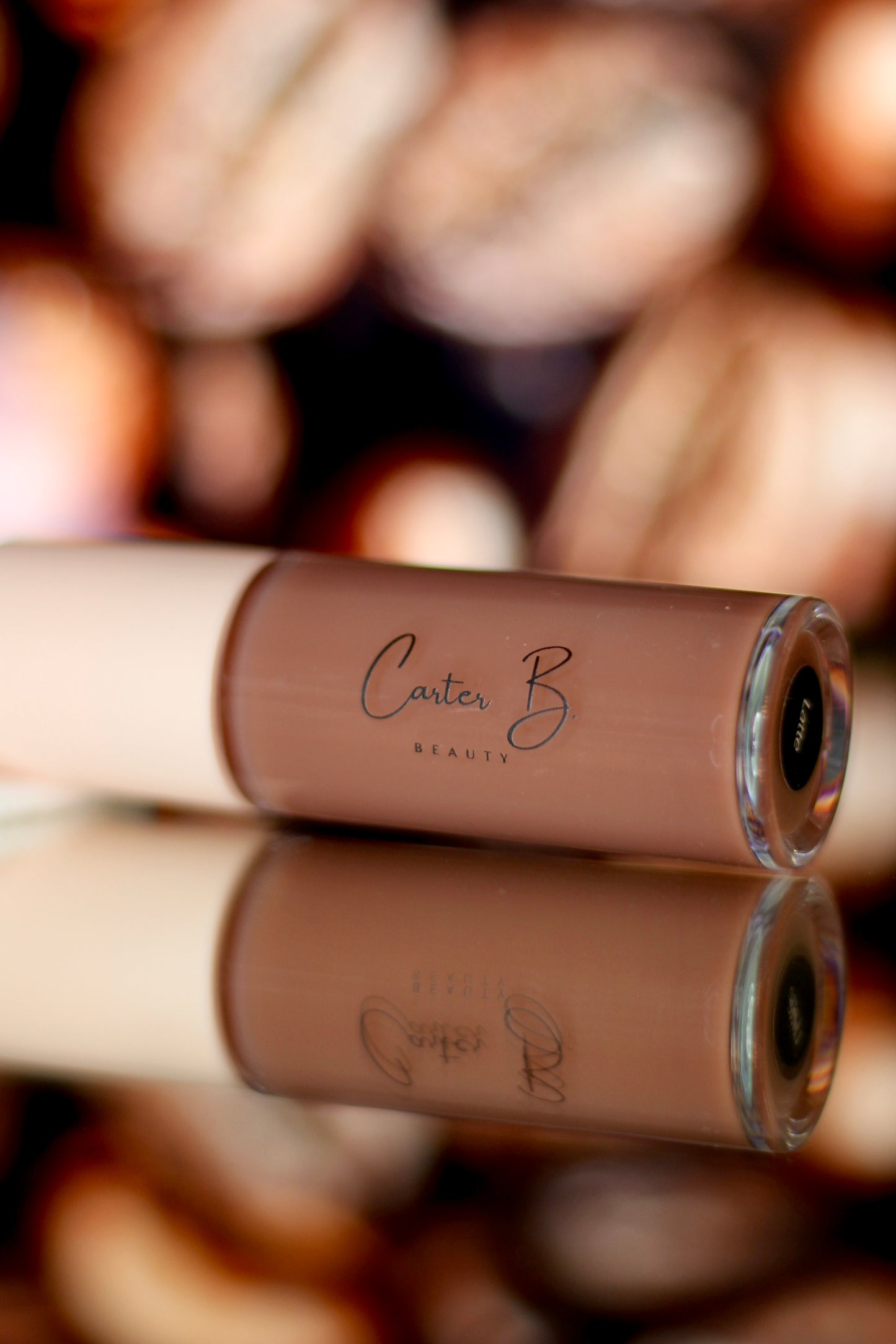 Carter B. Beauty Lippenöl in der Farbe LATTE – feuchtigkeitsspendendes, natürliches Lip Oil mit nudefarbenden Akzenten und pflegender Formel, präsentiert vor einem braunen Hintergrund. (liegend)