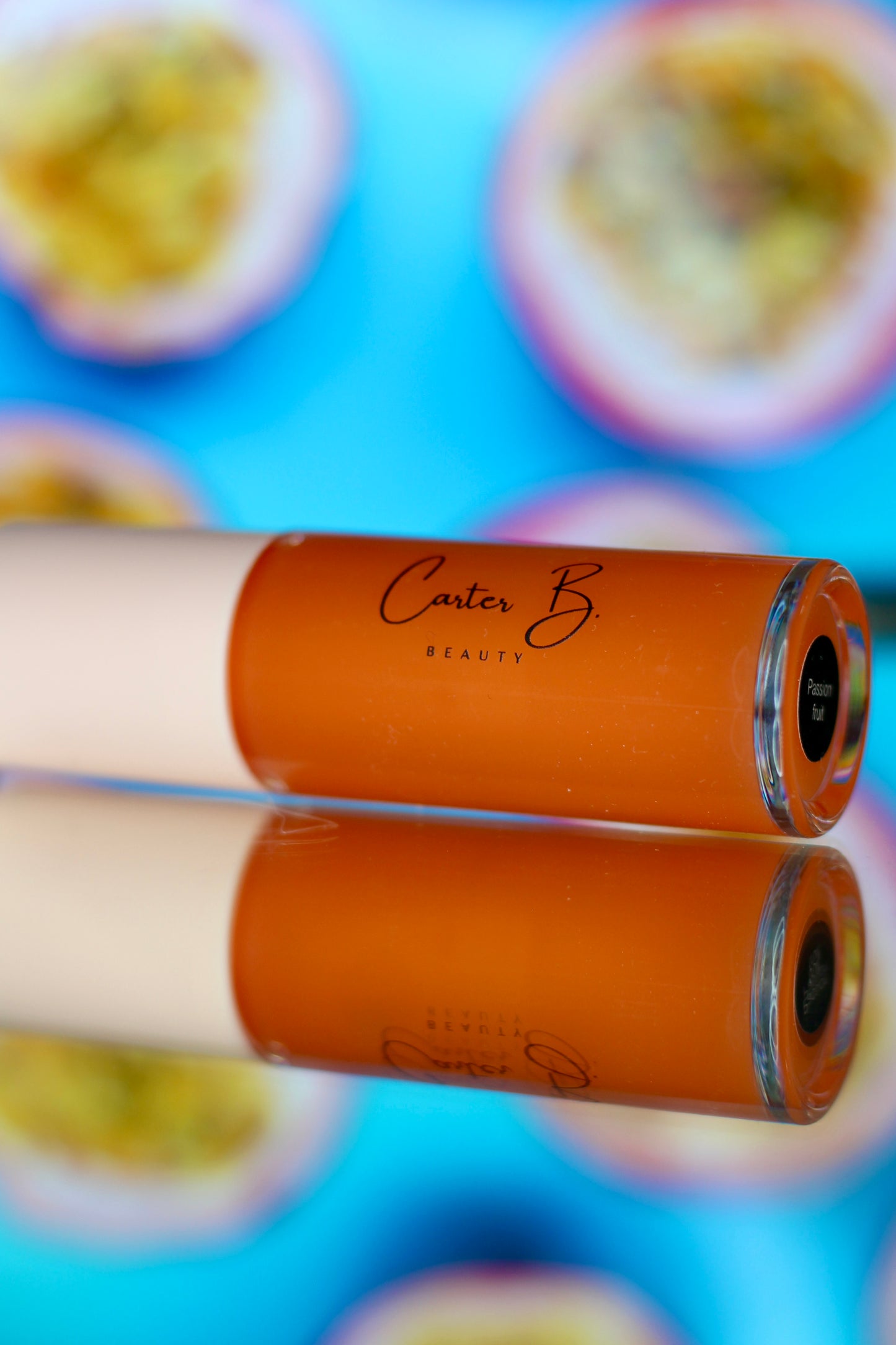 Carter B. Beauty Lippenöl in der Farbe PASSION FRUIT – feuchtigkeitsspendendes, natürliches Lip Oil mit orangen Akzenten und pflegender Formel, präsentiert vor einem tropischen Hintergrund. (liegend)