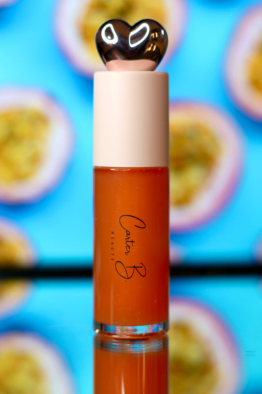 Carter B. Beauty Lippenöl in der Farbe PASSION FRUIT – feuchtigkeitsspendendes, natürliches Lip Oil mit orangen Akzenten und pflegender Formel, präsentiert vor einem tropischen Hintergrund. (stehend)